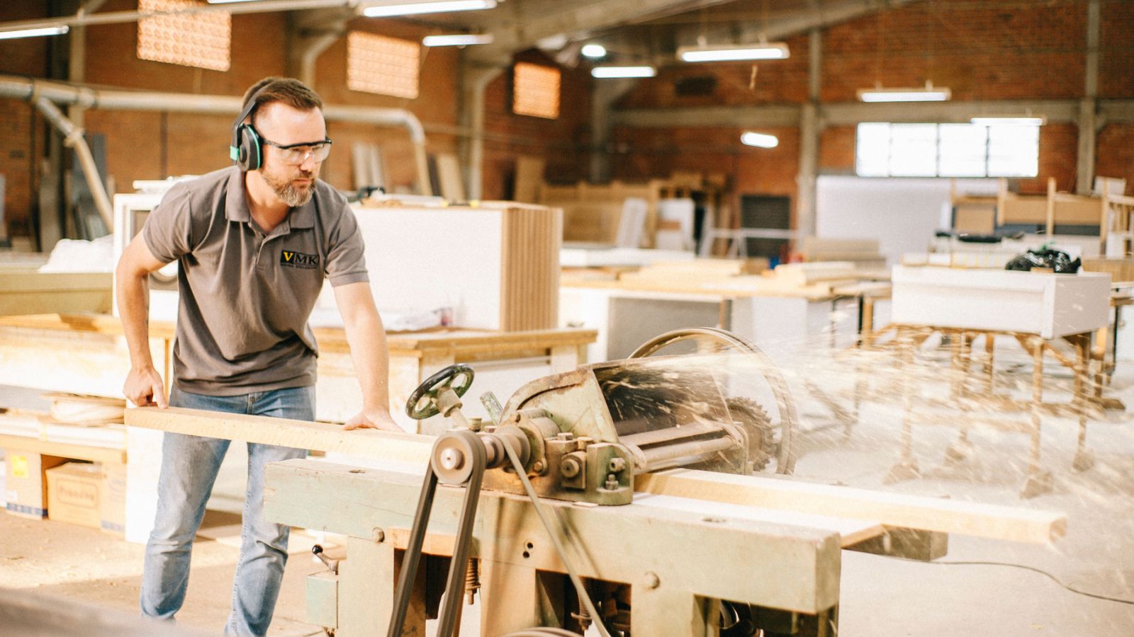 Carpenter operating woodworking machinery in a busy workshop.