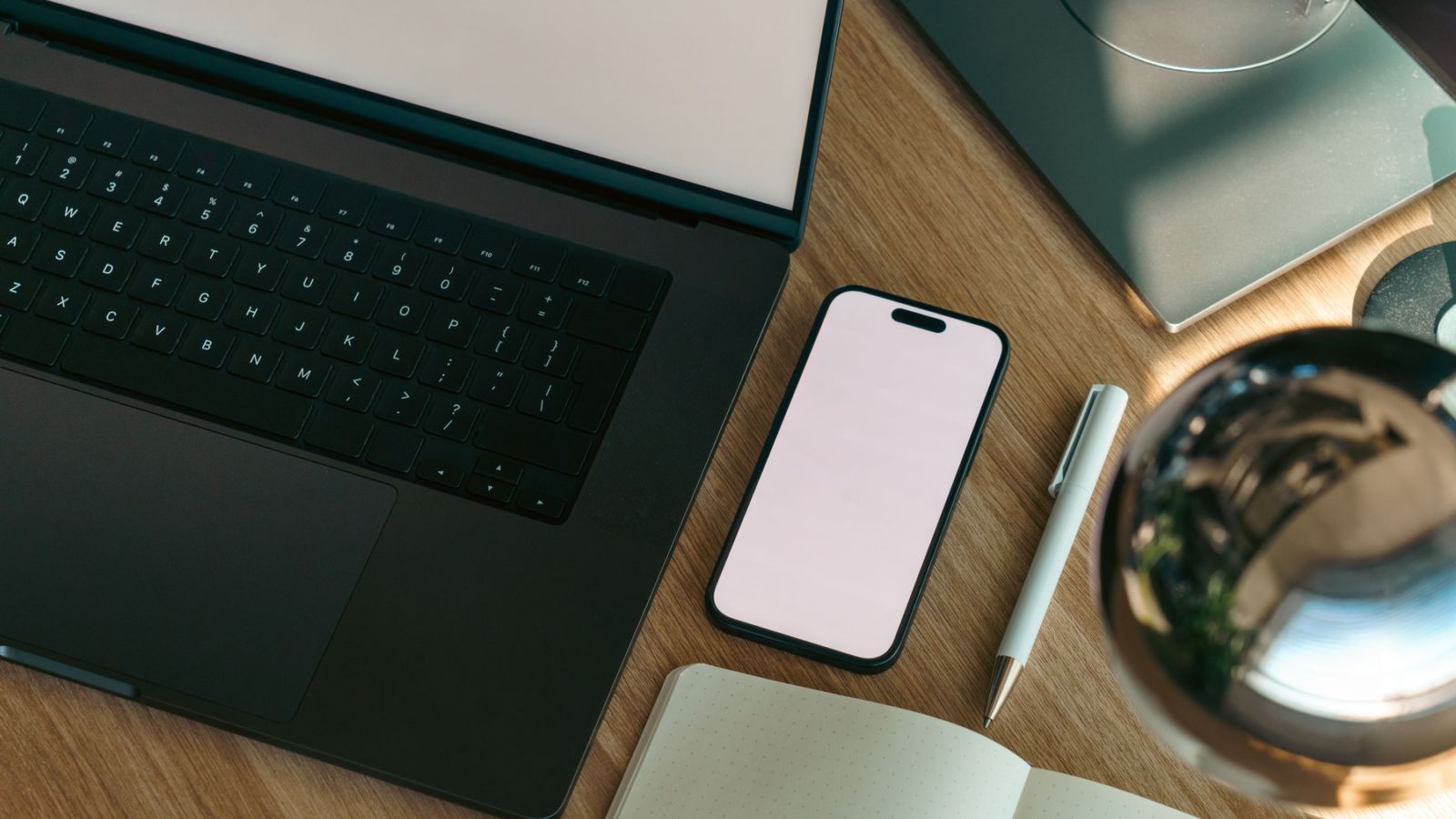 Top-down view of a laptop, smartphone, notebook and pen.