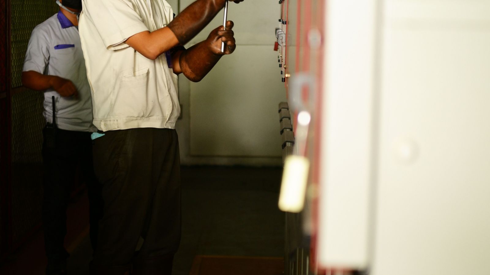 Electrician servicing electrical equipment while wearing safety gear.