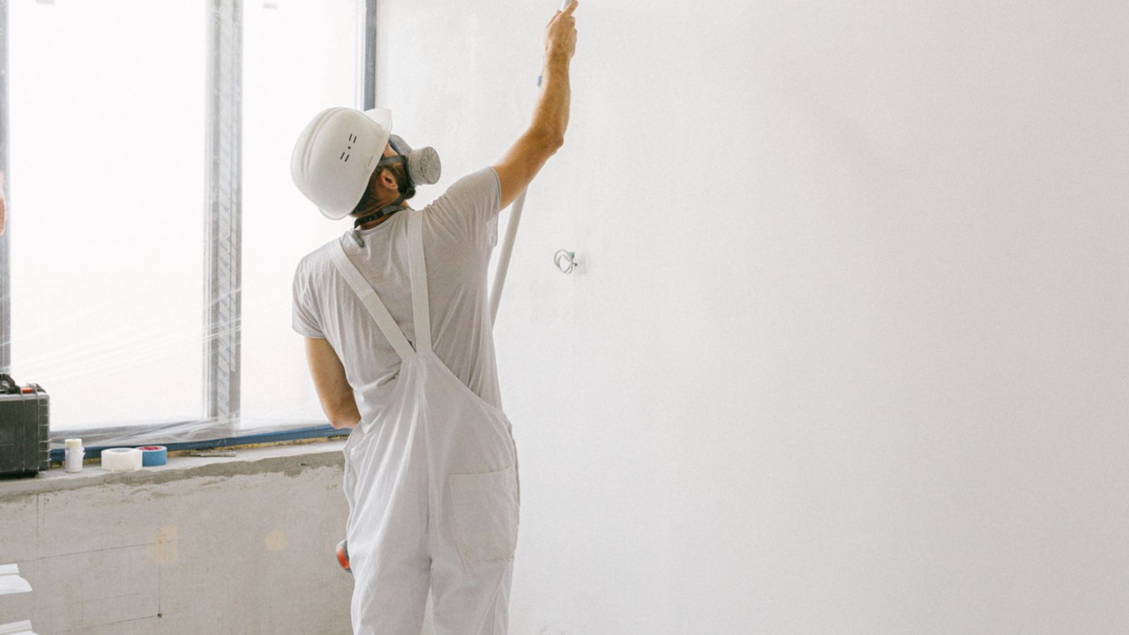 Professional painter applying white paint to an interior wall.